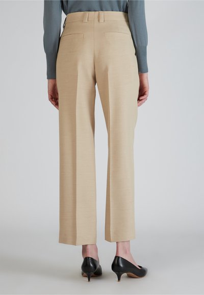 Beige high-waisted broek met een recht gesneden ontwerp, voorzien van twee achterzakken en een gladde textuur, gecombineerd met zwarte hakken.