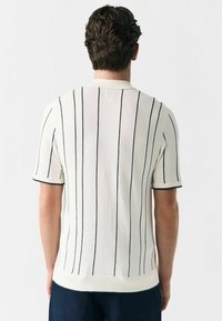 Short-sleeve, cream knit polo shirt featuring vertical navy stripes, a ribbed collar, and textured fabric.