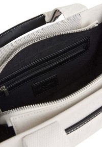 Kangaskassin sisäosa vaaleanharmaa mustilla vuorilla, jossa on vetoketjullinen tasku ja hopeinen vetoketju. Mustat nahkaosat.