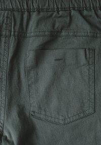 Mörkgröna tygshorts med elastisk midja, med en enda bakficka och kontrasterande sömmar. Mjuk textur.