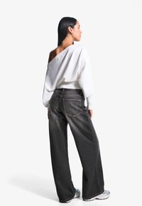 White off-shoulder sweater paired with loose-fitting dark gray jeans and silver sneakers, highlighting a relaxed silhouette and soft texture.