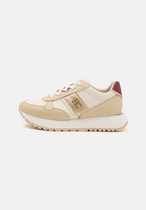 Sneaker in pelle beige con dettagli crema, chiusura bianca con lacci, texture tonali e tallone bordeaux. Presenta un logo prominente sul lato.