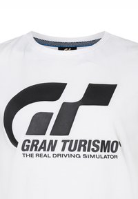 Camiseta de algodón blanca con un gran logo negro "GT" y el texto "GRAN TURISMO" con "EL VERDADERO SIMULADOR DE CONDUCCIÓN" debajo en negrita negra.