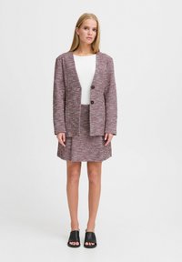 Tkaný materiál blazer a sukňový set v burgundskej, krémovej a sivej farbe. Blazer má dva gombíky; skombinovaný s bielym rebrovaným topom a čiernymi sandálmi.
