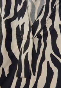 Mustekka ja valkoinen seeprahihallinen kangas, jossa on V-pääntie, keskeinen sauma ja pehmeä rakenne, sopii arkivaatteisiin.