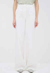 Witte wijde broek met een gladde textuur en een op maat gemaakte pasvorm, met een hoge tailleband en een schoon ontwerp. Zilveren schoenen zichtbaar.