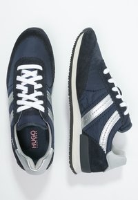 Ett par marinblå och silverfärgade Hugo Boss-sneakers med vita snörning, texturerade sulor och mocka-accenter, visade från ovan- och sidovy.