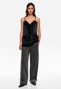 Camiseta de satén negra con encaje, combinada con pantalones de pierna ancha gris texturizados y zapatos negros de punta, con tirantes finos.