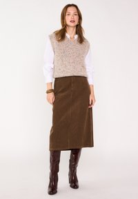 Veste en tricot duveteux rose clair portée sur une chemise blanche à col, associée à une jupe midi en velours côtelé marron et des bottes hautes bordeaux.