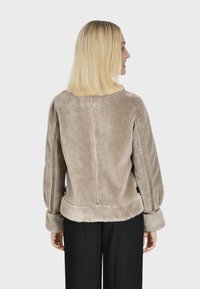 Beige nepbont jasje met een zachte textuur, ronde halslijn en wijde mouwen. Heeft een rechte rugnaad en zachte, gezoomde manchetten.