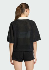 Čierny sieťovaný top s voľným strihom, s rebrovaným okrúhlym výstrihom a krátkymi rukávmi. Nosený s rovnakými čiernymi šortkami.