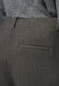 Mörka herringbone-byxor med en slät yta, som har en enda bakficka och en skräddarsydd passform, kombinerat med en grå stickad tröja.