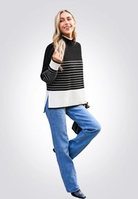 Schwarz-weiß gestreifter Pullover mit hohem Kragen, kombiniert mit hellblauen weit geschnittenen Jeans und schwarzen Stiefeletten.