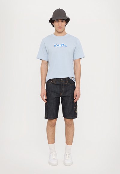 Light blue cotton t-shirt with printed logo, paired with dark denim shorts featuring contrasting stitching and side pockets. White sneakers complete the look.