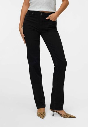 Jeans de mezclilla negra con un ajuste slim, diseño de cinco bolsillos y una cintura de altura media, combinados con tacones de serpiente de punta.