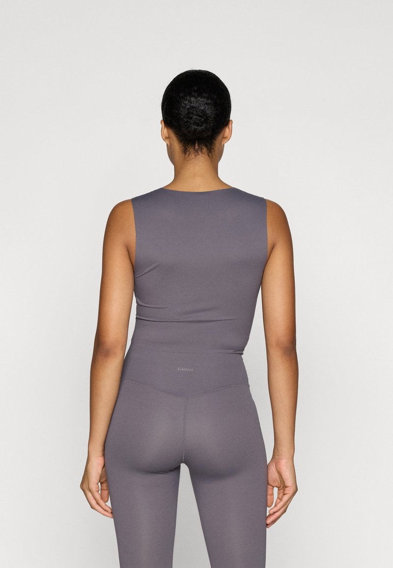 Top sin mangas gris y leggings de tiro alto, ambos en un material suave y elástico. Presentan un diseño ajustado y un sutil logo de la marca en la parte posterior.