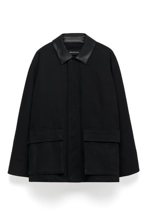 Zwarte jas van katoen met een leren kraag. Voorzien van twee grote voorzakken en een knoopsluiting. Oversized ontwerp en rechte snit.