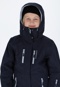 Ciemnoniebieska kurtka narciarska o teksturowanym wykończeniu, z regulowanym kapturem i szarymi zamkami błyskawicznymi. Posiada logo z przodu oraz dwie kieszenie zapinane na zamek.