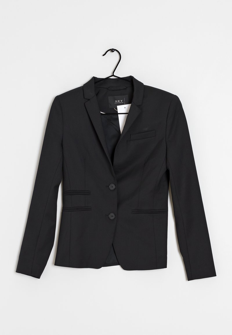 Blazer noir pour femme sur mesure avec deux boutons, col à revers cranté et trois poches avant, suspendu sur un cintre noir sur fond blanc.