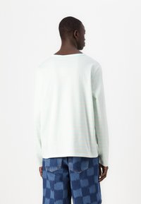 Light blue long-sleeve shirt with subtle vertical stripes, crew neck, soft fabric, paired with blue patterned jeans.