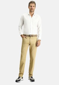 Outfit da uomo composto da una camicia bianca con bottoni, pantaloni color khaki e sneakers nere e grigie. La cintura è caratterizzata da una texture con un design intrecciato.