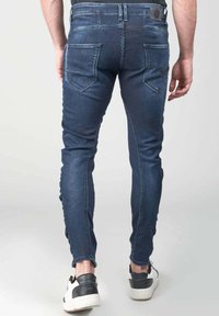 Vaqueros ajustados en denim azul oscuro, con una textura deslavada, cinco bolsillos y un sutil parche con el logo en la cintura.
