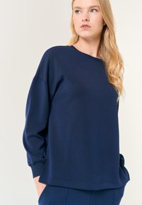 Maglietta a maniche lunghe blu navy con vestibilità rilassata, dotata di polsini a coste e di un motivo testurizzato sulla superficie. Design semplice con collo a giro.