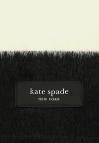 Black and white fuzzy fabric with a black rectangular label displaying "kate spade NEW YORK" in white text.