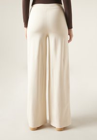 Pantalons larges en crème, fabriqués en tissu lisse et extensible. Dotés d'une taille haute et d'ourlets nets, offrant une coupe décontractée.