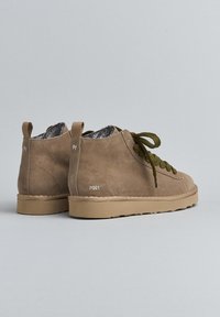 Par de botas de ante beige hasta el tobillo con cordones verde oliva y suelas de goma marrón claro sobre un fondo gris liso.