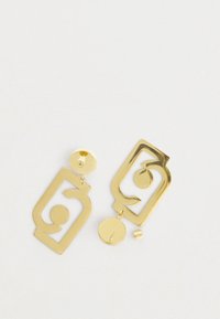 Ζευγάρι χρυσών γεωμετρικών σκουλαρικιών με αφηρημένο σχέδιο σπείρας σε λευκό φόντο, ένας σφικτήρας σκουλαρικιού αποσπασμένος.