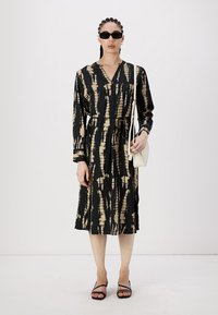 Juoda ir kreminė suknelė su ilgu rankovėm, V formos iškirpte ir diržu liemeniui. Dėvima su juodais saulės akiniais ir minimaliais aksesuarais.