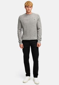 Szary sweter dziany z wzorem w warkocze, okrągłym dekoltem i ściągaczami, w zestawie z czarnymi spodniami i białymi sneakersami.