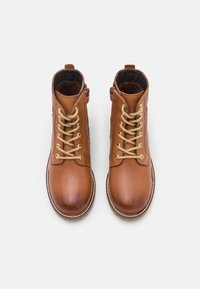 Botas de tobillo de cuero marrón con un acabado suave, ojales dorados y cordones en marrón claro. Punta redondeada y detalle de suela cosida.