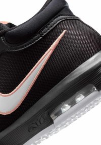 Gros plan du talon d'une chaussure de sport noire avec un logo swoosh brodé blanc et rose et une semelle à coussin d'air visible.