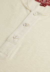 Camisa henley de algodón color crema con un tapanchise de tres botones, textura sutil y un cuello redondo con costuras reforzadas.