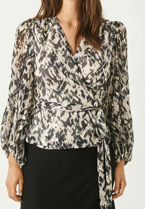 Blouse légère enroulée avec un imprimé animal noir, blanc et doré. Manches longues bouffantes, taille cintrée et détail à nouer sur le côté.