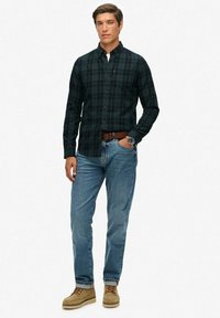 Heren donkergroene geruite shirt met lange mouwen, gedragen met lichtblauwe jeans en tankleurige boots. Voorzien van een knoopsluiting kraag en een getailleerde pasvorm.
