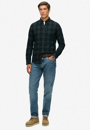 Men's dark green plaid shirt with long sleeves, paired with light blue jeans and tan boots. Features a button-down collar and fitted cut.