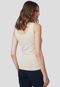 Beżowy top na ramiączkach o dopasowanym kroju, z szerokimi ramiączkami i gładką bawełnianą fakturą. Na plecach znajduje się subtelne logo.