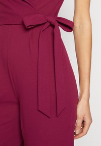 El mono burdeos presenta una cintura ajustada con un detalle de lazo, una tela suave y una silueta elegante.