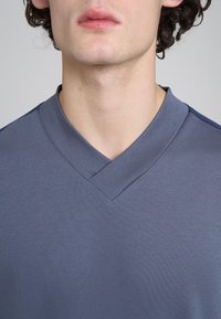 Maglietta blu scuro a V realizzata in tessuto morbido; presenta una leggera texture e un colletto angolato per un design moderno.