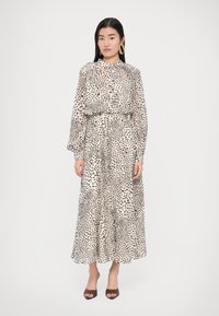 Hosszú, bő szabású ruha, könnyű, áttetsző anyagból, amely krémszínű alapon fekete pöttyös mintázattal rendelkezik. Hosszú ujjú és magas gallérú.