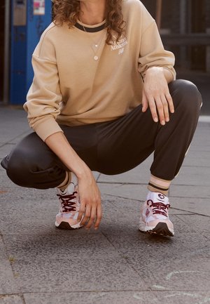 Beige tröja med svart krage, svarta byxor och rosa träningsskor med röda detaljer. Snygg textur och avslappnad passform.