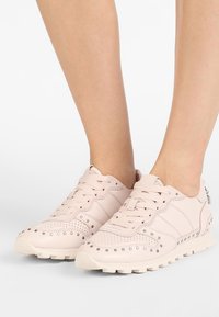 Světle růžové tenisky vyrobené z kůže s perforovanými detaily, šněrováním, zaoblenou špičkou a gumovou podrážkou; stříbrné akcenty po stranách.