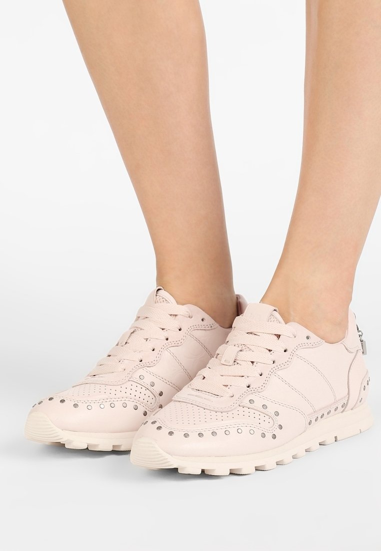 Světle růžové tenisky vyrobené z kůže s perforovanými detaily, šněrováním, zaoblenou špičkou a gumovou podrážkou; stříbrné akcenty po stranách.