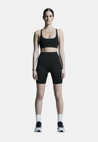 Mustat urheilulliset cropped topit ja korkeavyötäröiset shortsit, valmistettu joustavasta ja sileästä kankaasta, yhdistetty valkoisiin nilkkasukkasiin ja mustiin juoksukenkien.