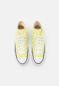 Limetkově žluté plátěné vysoké tenisky s bílými tkaničkami, gumovými špičkami a černými bočními akcenty. Hladký povrch bez viditelných vzorů.