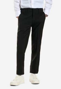 Pantalones negros de corte ajustado con una textura suave, que cuentan con bolsillos laterales y un ajuste ceñido. Combinados con zapatillas blancas y una camisa blanca de botones.