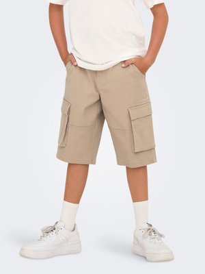 Beige cargo shorts with two large side pockets and a relaxed fit, paired with white sneakers and crew socks. Cotton material, casual design.